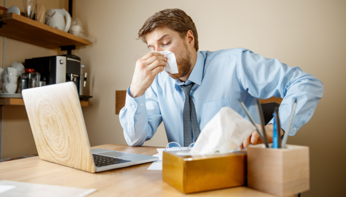 sick-man-with-handkerchief-sneezing-blowing-nose-while-working-office